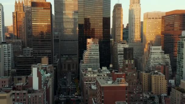 Adelante vuelan por encima de edificios en el centro de la ciudad. Rascacielos modernos con fachadas brillantes que reflejan el cielo colorido del atardecer. Manhattan, Nueva York, Estados Unidos - Metraje, vídeo
