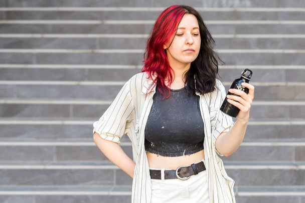 Portrait of young stylish woman with steel eco bottle in hand, wearing casual clothes - Photo, Image