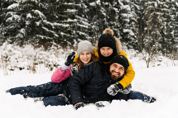 Happy family have fun in winter forest and looking at camera. Mother, father and son playing with snow. Family Christmas concept. Enjoying spending time together - 写真・画像