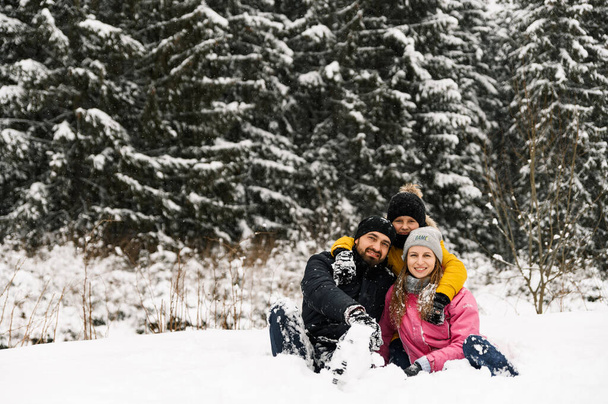 Happy family have fun in winter forest and looking at camera. Mother, father and son playing with snow. Family Christmas concept. Enjoying spending time together - Valokuva, kuva