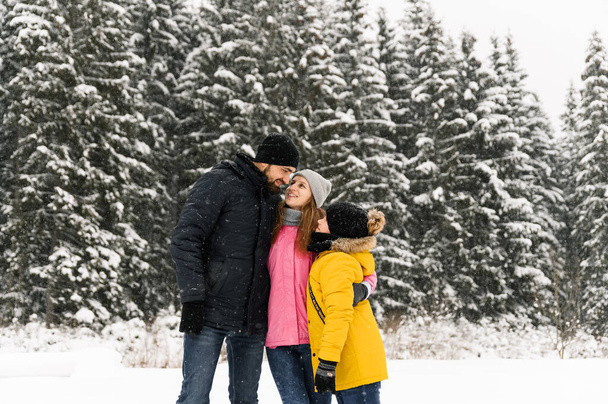 Happy family have fun in winter forest and looking at camera. Mother, father and son playing with snow. Family Christmas concept. Enjoying spending time together - Photo, Image