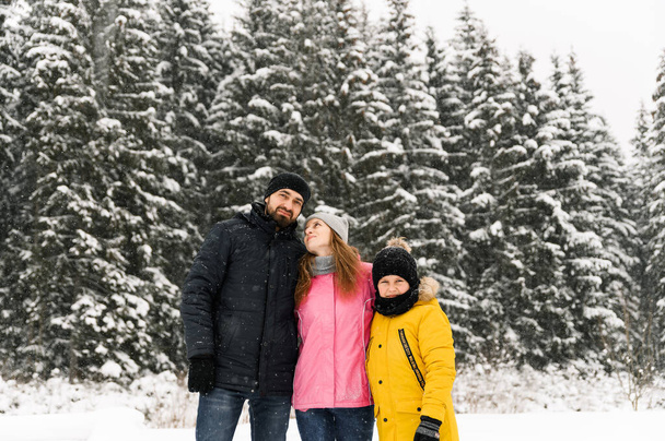 Happy family have fun in winter forest and looking at camera. Mother, father and son playing with snow. Family Christmas concept. Enjoying spending time together - Foto, afbeelding