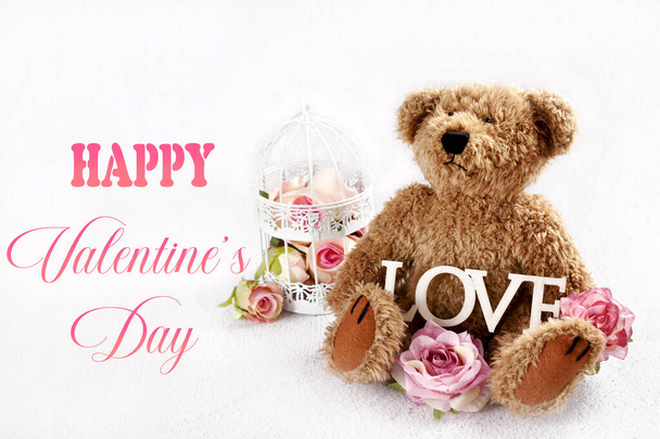 Valentines card with cute teddy bear with with roses and wooden LOVE inscription sitting on white background with empty copy space on left - Foto, imagen
