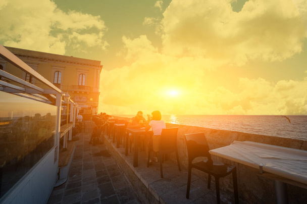 Gallipoli, Puglia, Olaszország. 2021. augusztus. A naplemente csodálatos atmoszférája varázslatossá teszi az aperitif pillanatot. Az emberek bárokba és éttermekbe járnak, hogy élvezzék.. - Fotó, kép