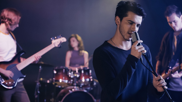 young singer performing song with blurred music band - Fotoğraf, Görsel