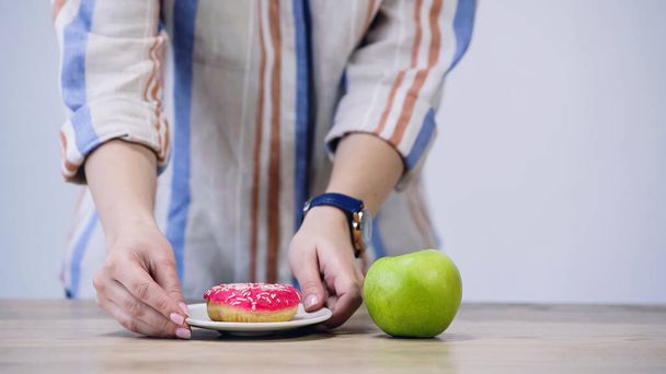 cropped view of woman holding plate with doughnut near apple isolated on grey - Photo, Image