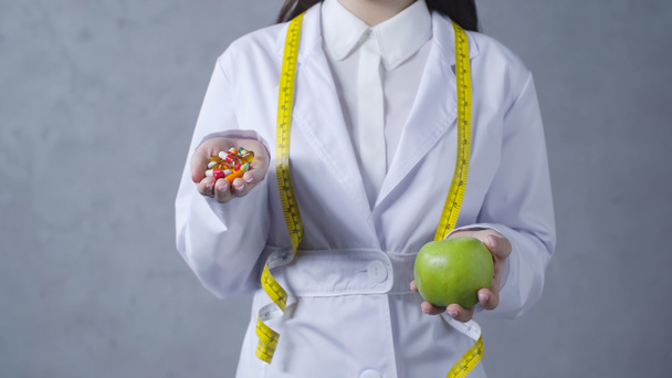 partial view of nutritionist comparing apple and vitamins on grey  - Fotó, kép