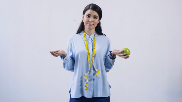mujer confundida comparando vitaminas y manzana aislada en gris - Foto, Imagen