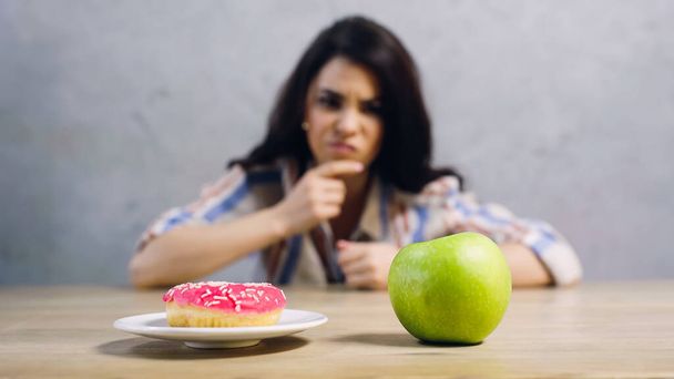 blurred woman choosing between apple and doughnut on grey - Фото, изображение