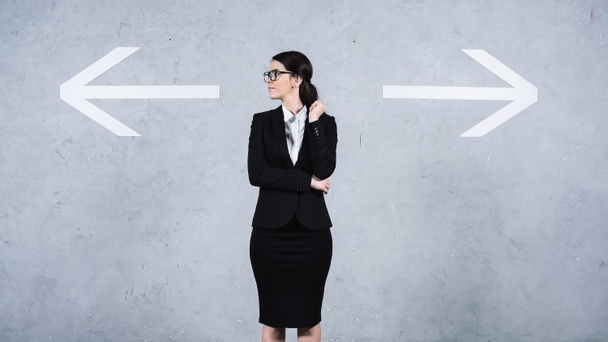 businesswoman in glasses looking away near arrows on grey - Photo, Image