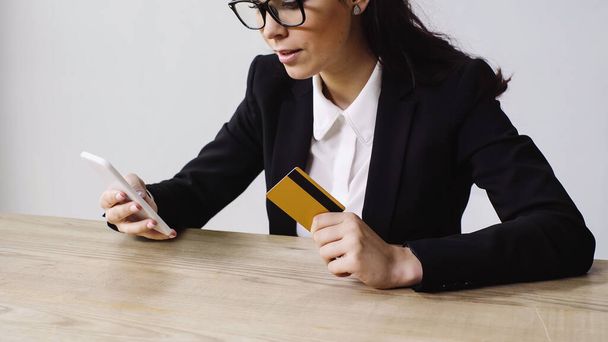 brunette businesswoman holding smartphone and credit card isolated on white  - Foto, Bild