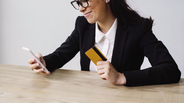 cheerful businesswoman doing online shopping while holding smartphone and credit card isolated on white  - 写真・画像