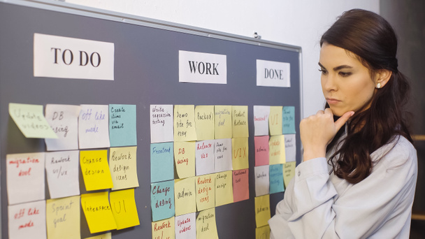 pensive businesswoman thinking near colorful sticky notes on board - Foto, Imagem