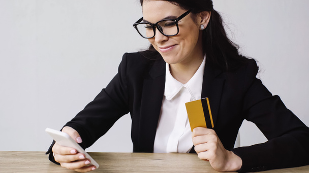 pleased businesswoman holding smartphone and credit card isolated on white  - Valokuva, kuva