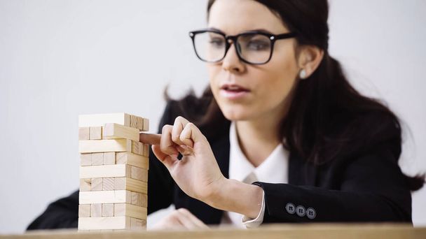 blurred brunette businesswoman playing blocks wood tower game isolated on grey  - Foto, immagini