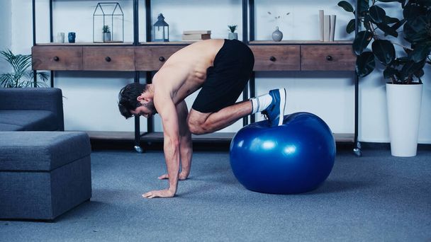 side view of muscular sportsman training with fitness ball at home - Foto, immagini