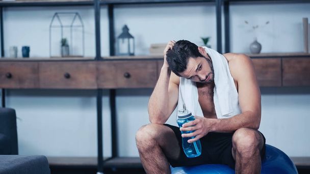 deportista cansado con toalla sentado en la pelota de fitness y la celebración de la botella de deportes  - Foto, Imagen