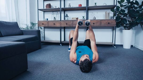 young sportsman lying on floor and training with dumbbells - Foto, Imagem