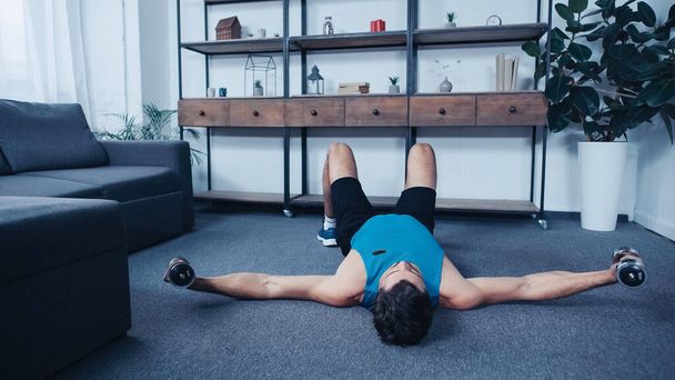 young sportsman lying on floor and exercising with dumbbells - 写真・画像