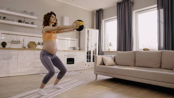 Pregnant woman training with slam ball at home  - Foto, afbeelding