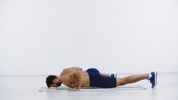 bearded sportsman exercising on fitness mat near white brick wall - 写真・画像