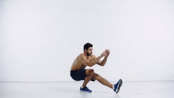 bearded sportsman in shorts and sneakers working out near white brick wall - Foto, Imagem