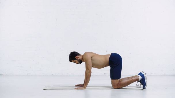 boční pohled na vousatý sportovec dělá zpět cvičení v blízkosti bílé cihlové zdi  - Fotografie, Obrázek