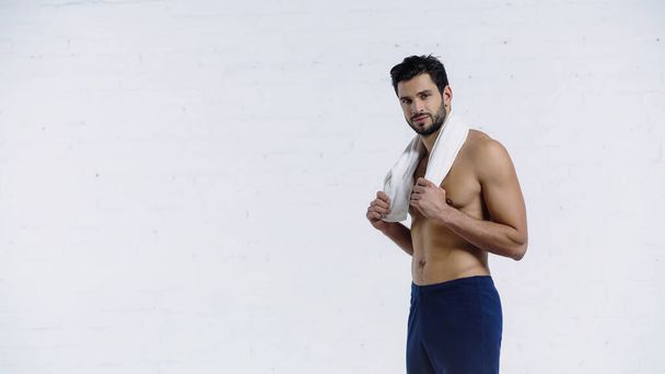 hombre deportivo sosteniendo la toalla y sonriendo mientras mira a la cámara en blanco - Foto, imagen