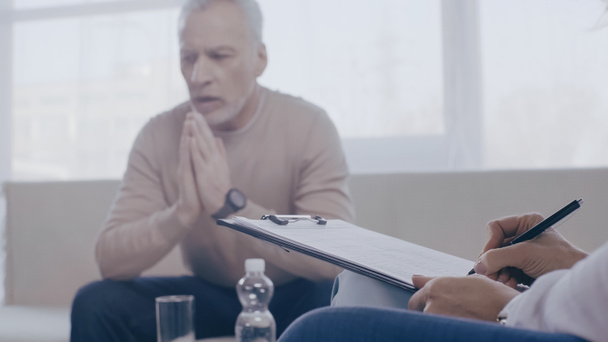 psycholoog schrijven op klembord bijna wazig middelbare leeftijd patiënt praten tijdens overleg  - Foto, afbeelding