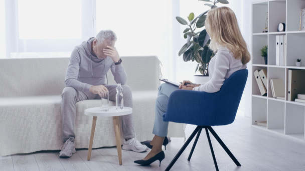 depressed mature sportsman and blonde psychologist having conversation in consulting room - 写真・画像