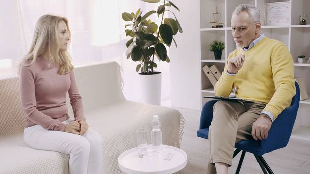 psicólogo pensativo y maduro teniendo conversación con paciente rubia  - Foto, Imagen