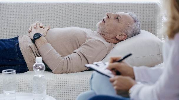 розмитий психолог пише на кишені біля пенсіонера середнього віку, який лежить на дивані під час терапії
  - Фото, зображення