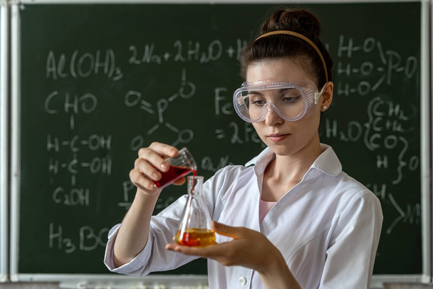 Νεαρή γυναίκα επιστήμονας με λευκό παλτό και γυαλιά που κρατά εργαστηριακή φιάλη - Φωτογραφία, εικόνα