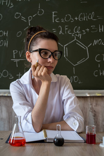 Γυναίκα καθηγητής χημείας αναμιγνύει υγρά σε μια γυάλινη φιάλη με μαυροπίνακα με χημικό τύπο - Φωτογραφία, εικόνα