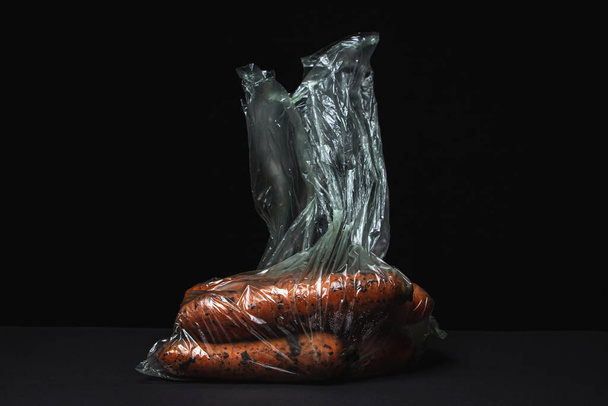 Carrots on a black background. Carrots in a plastic bag on a dark background. Healthy vegetables - Photo, image