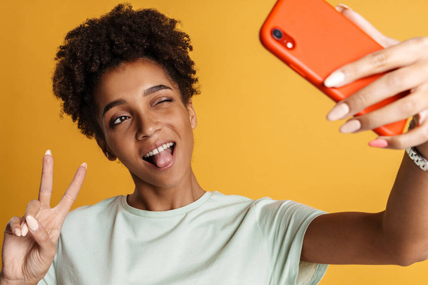 Young black woman smiling while using mobile phone isolated over yellow background - Fotografie, Obrázek