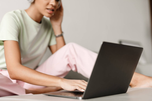 Young black woman in headphones using laptop while sitting on couch at home - Photo, Image