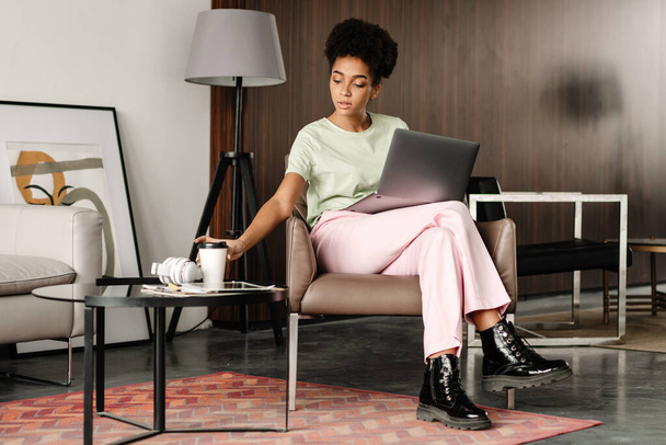 Young black woman drinking coffee while working with laptop at home - Photo, image