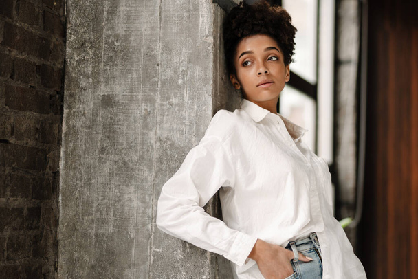 Young black woman leaning on wall and looking aside indoors - Foto, Bild