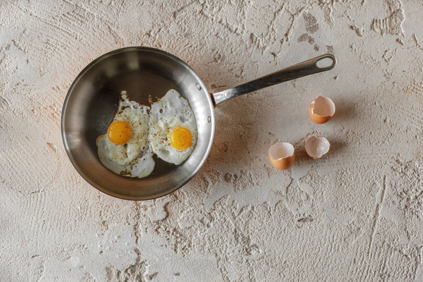 Fried two eggs in copper pan on rough textured clay background. Healthy breakfast concept. - Photo, Image