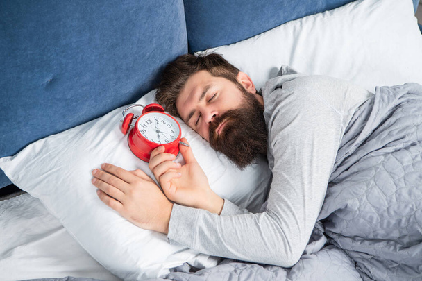 Sleepy man with alarm clock being in bed asleep, sleep time - Фото, изображение