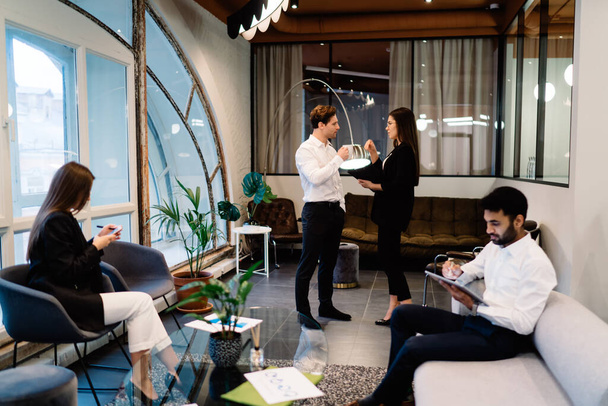 Side view of young multiracial businesspeople using tablet and smartphone while discussing job in contemporary convenient workspace with potted plants - Fotografie, Obrázek