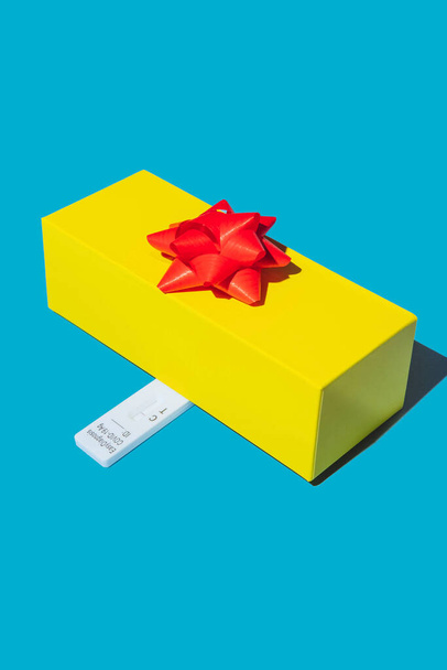 Una confezione regalo gialla con un test rapido COVID-19 negativo su sfondo blu. - Foto, immagini