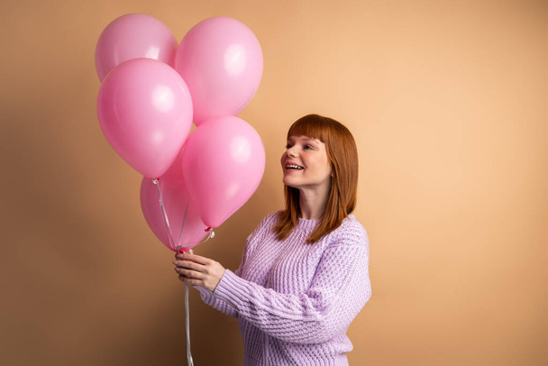 Portrait of positive cheerful girl holding balloons got for anniversary, having free time with friends, listening funny jokes, laughing isolated orange color background  - Фото, изображение