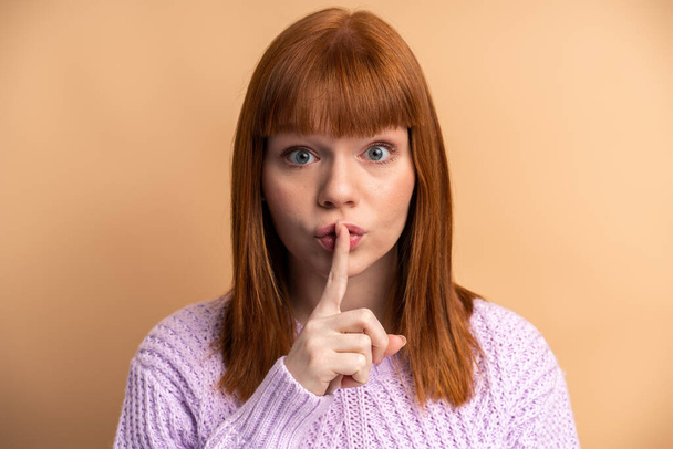Будь спокійним. Портрет серйозної жінки, що показує жест мовчання пальцем на роті, з проханням мовчати, зберігати таємницю. Внутрішній студійний знімок ізольований на помаранчевому фоні
  - Фото, зображення