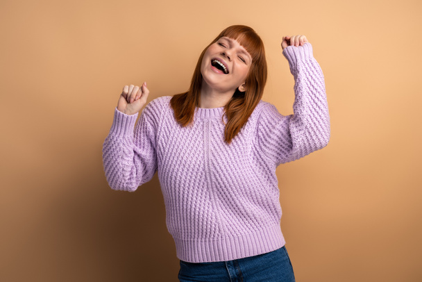Positive satisfied woman raised clenched fists, being happy of winning, expressing triumph. Indoor studio shot isolated on orange background  - Foto, Bild
