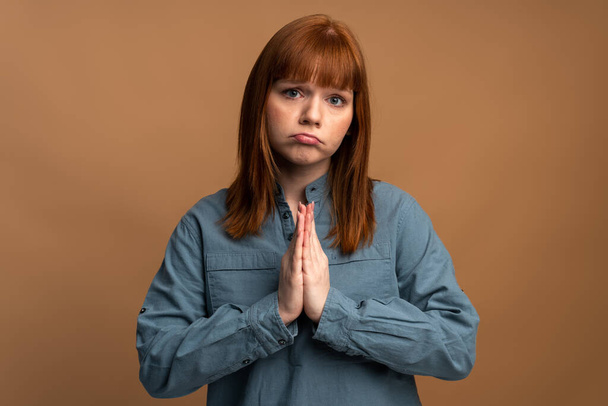 Portrait of young attractive woman looking at the camera with imploring desperate grimace, praying to god asking for help. Indoor studio shot isolated on orange background  - Foto, imagen
