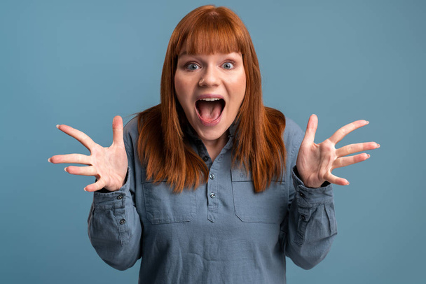Wow, I can't believe this. Portrait of astonished woman with widely open mouth in amazement and big eyes looking at camera, stunned shocked face. Indoor studio shot isolated on blue background  - Foto, imagen