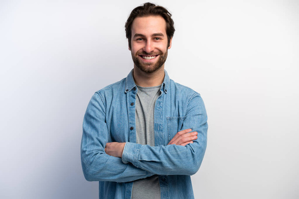 Image of happy brunette man wearing basic clothes smiling at camera with hands crossed isolated over white background. Stock photo  - Fotografie, Obrázek
