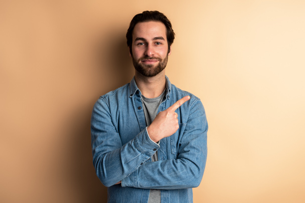 Portrait of positive friendly brunette man with beard standing and pointing at right, empty space for text, advertise. Indoor studio shot isolated on orange background  - Foto, Imagem